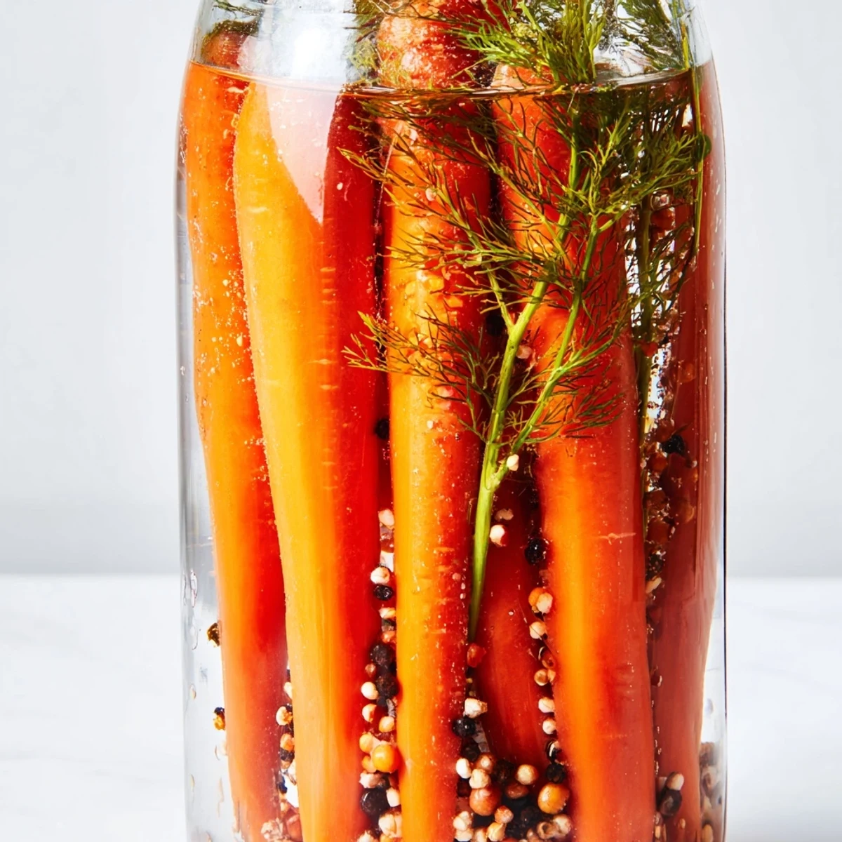 Quick pickled carrot spears glistens in a jar, showcasing the vibrant colors and tangy, crisp texture.