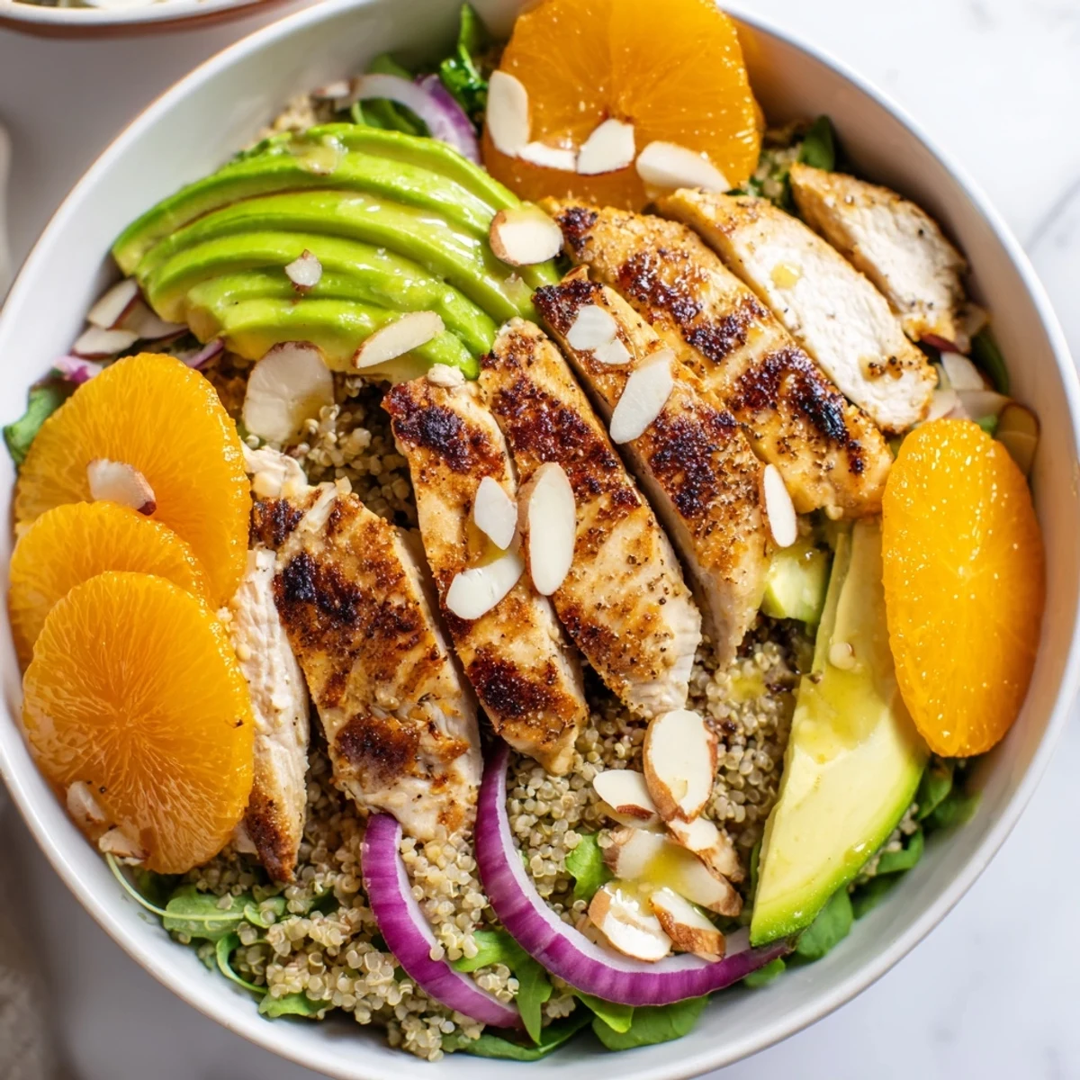Grilled herb chicken sits atop a vibrant Citrus Herb Chicken Salad Bowl with avocado and orange segments.