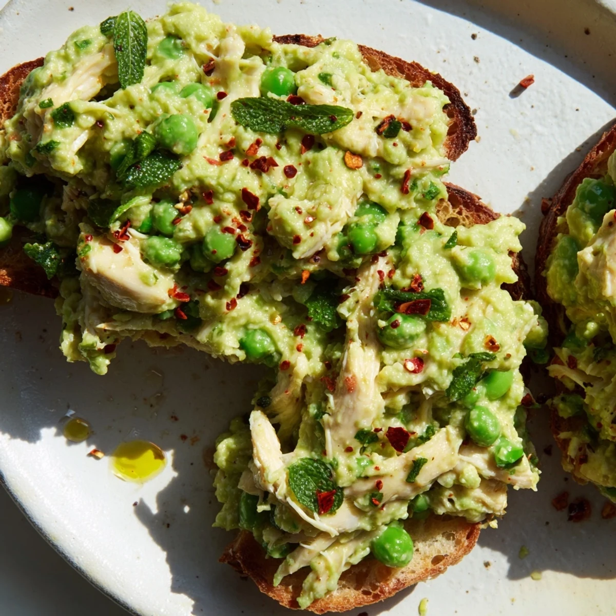 A vibrant Smashed Pea & Chicken Toast topped with chili flakes and fresh herbs.