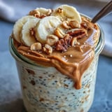 Close-up of creamy High-Protein Peanut Butter Overnight Oats topped with sliced bananas, chopped peanuts, and a honey drizzle. 