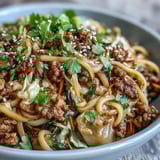 A close up of a steaming potsticker noodle bowl features ground pork, shredded cabbage, and carrots tossed in a glossy soy sauce.