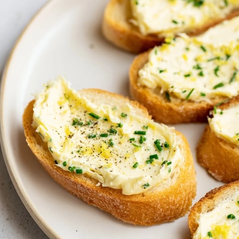 Golden-brown vodka butter crostini arranged on a rustic wooden board with fresh chives and lemon zest.