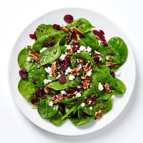 A vibrant Spinach Goat Cheese Salad with creamy crumbles, sweet cranberries, and crunchy candied pecans tossed in tangy balsamic vinaigrette.