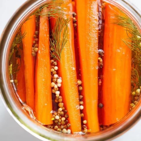 Close-up of freshly made quick pickled carrot spears ready for snacking, with visible spices throughout.
