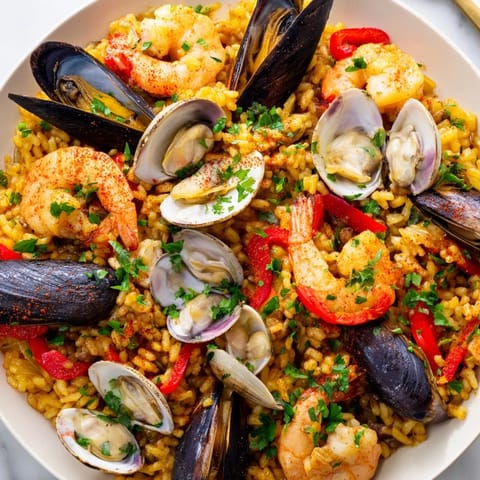 A close-up of a steaming pan of delicious Spanish Seafood Paella overflowing with shellfish and saffron rice.