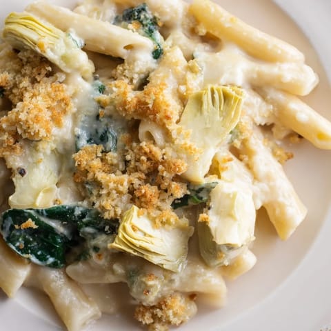 A close-up of Artichoke Pasta Bake in a ceramic dish, showcasing tender pasta, marinated artichoke hearts, and fresh spinach in rich sauce.