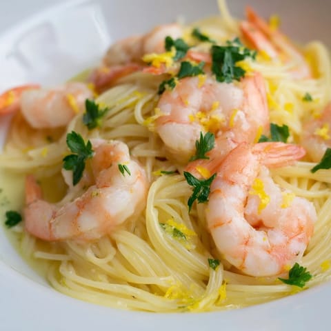 Savory Lemon Butter Shrimp Pasta Lite served in a white bowl, garnished with lemon wedges and parsley on a rustic wooden table.