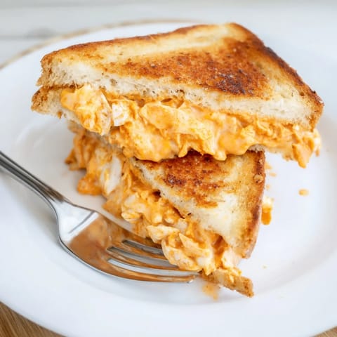 Toasted sourdough bread with melted cheese and buffalo chicken on a rustic wooden cutting board.