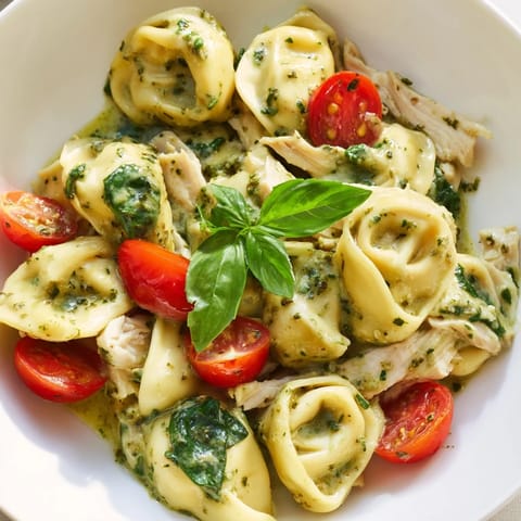 Golden-brown tortellini and shredded rotisserie chicken simmer in a creamy pesto sauce in a hot skillet.
