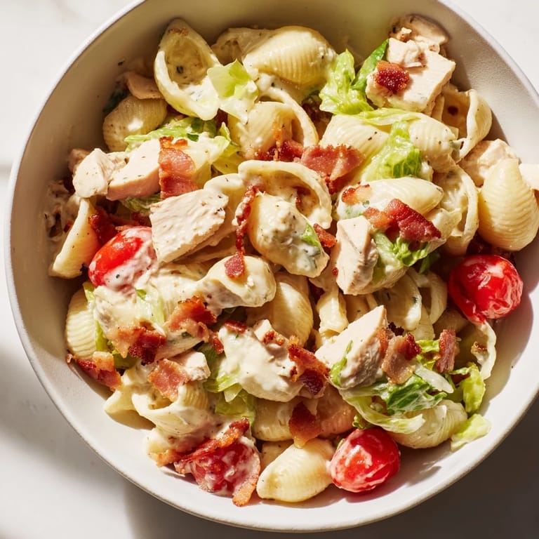 A hearty serving of BLT Chicken Pasta Salad on a rustic plate with visible pasta shells and juicy tomato halves.